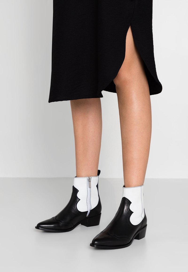 Jambes inférieures portant des bottines en cuir noir et blanc avec des fermetures éclair latérales et une jupe noire fendue devant.