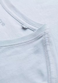 Valkoinen puuvillapaita, jossa on pyöreä kaula-aukko, hienosti ribatukset reunat ja näkyvä ompelu. Sileä pinta ja puhdas viimeistely.