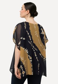 Maglietta trasparente tie-dye nera e dorata con vestibilità rilassata e maniche a pipistrello, caratterizzata da motivi ondulati e una texture fluida.