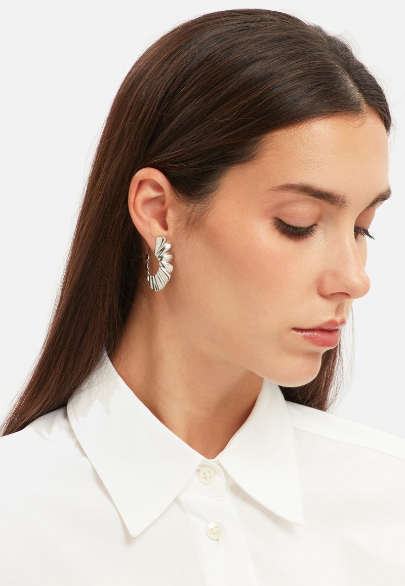 Zilveren creolen met een textuur die lijkt op bladeren. De oorbellen zijn van gemiddelde grootte en hebben een gepolijste afwerking.