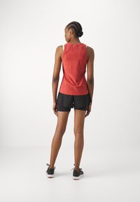 Red sleeveless top, fitted design, smooth texture, paired with black shorts, athletic style, worn with black sneakers. Plain background.