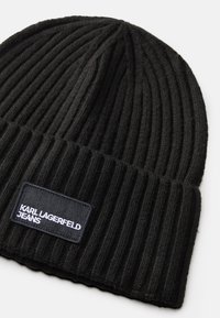 Fekete, bordás kötött sapka hajtott szélekkel, amelyen egy téglalap alakú fekete címke van varrva, fehér "Karl Lagerfeld Jeans" felirattal.