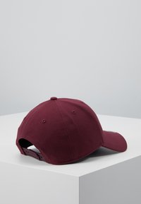 Burgunder baseballcap laget av stoff med en buet skygge, justerbar stropp bak og sømdetaljer på overflaten.
