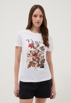 Joven mujer con una camiseta blanca con la palabra "Flower" y un gran estampado floral detallado, combinado con pantalones cortos negros.
