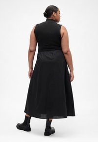 Schwarzes ärmelloses Kleid mit tailliertem Oberteil und fließendem Maxirock. Der Stoff ist glatt und betont das Rückendesign sowie die Silhouette.