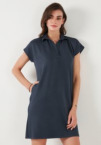 Navy polo dress made of smooth fabric, featuring short sleeves, a collared neckline, and side pockets; simple and streamlined design.