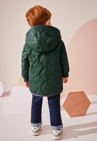 Grön vadderad jacka med huva, med böjda söm-mönster. I kombination med mörka jeans och retro-stil sneakers.