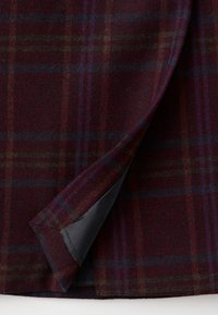Plaid fabric with dark burgundy base, featuring green, blue, and purple stripes. Soft texture with a contrasting black lining visible.