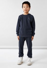 Sweatshirt et sweatpants bleu marine foncé en tissu doux, avec un petit logo. Complété par des baskets montantes blanches.