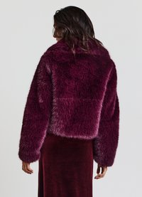 Veste en fausse fourrure bordeaux avec un design court, des manches larges et une texture douce. Présente un col haut et sans fermetures visibles.