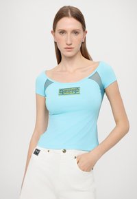 Light blue short-sleeve top with a scoop neckline, featuring sheer mesh accents on the shoulders and a decorative patch in the center.