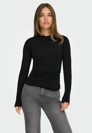 Schwarzes Langarmoberteil mit einer taillierten Form und geraffter Textur an den Seiten. Es hat einen runden Halsausschnitt und gerippte Ärmelabschlüsse, kombiniert mit grauen Jeans.