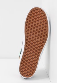 Semelle de basket blanche avec un motif en caoutchouc marron texturé, présentant un design géométrique. Le côté affiche des accents colorés et une couture détaillée.