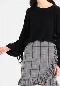 Svart, texturerad tröja med ballongärmar, matchad med en volangprydd, rutig kjol i svart och vitt, med en fransad nederkant.