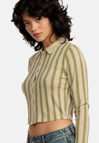 Camisa corta con cuello en color beige, con rayas verticales en verde y azul. Tejido texturizado con cierre de botón en la parte delantera y mangas largas.