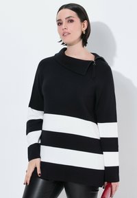 Zwart-wit gestreepte trui met hoge kraag, met ritsdetail op de schouder. De stof heeft een gladde, gestructureerde afwerking.