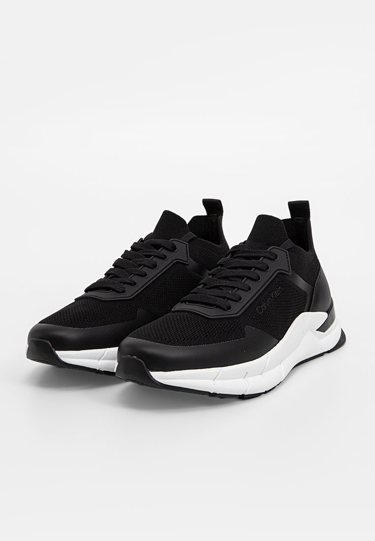 Baskets noires avec une tige en tricot texturé et des accents noirs lisses. Comprend une semelle blanche au design angulaire et un système de laçage à l'avant.