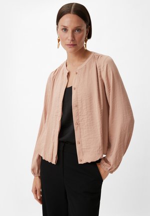 Light pink, long-sleeve button-up shirt in crinkled fabric with a round neckline and elastic cuffs, worn over a black top and black pants.