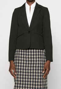 Černý krátký blazer s upravenými klopami, s jedním knoflíkem vpředu a postranními kapsami, kombinovaný s kostkovanou sukní v krémové a námořnické barvě.