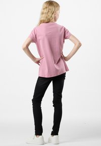 T-shirt in cotone rosa con maniche corte e una forma leggermente svasata, abbinata a jeans skinny neri e sneakers bianche.