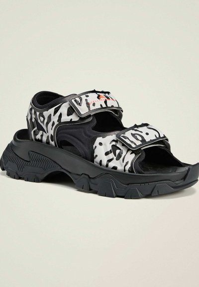 Zwart-wit gemusterde sandalen met een open teenontwerp; verstelbare banden, profieldan en een dikke, robuuste zwarte loopzool.