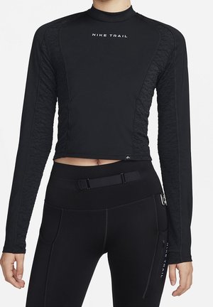 Personne portant un crop top noir Nike Trail à manches longues et des leggings taille haute noirs avec ceinture et poche zippée.