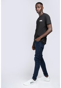 Sort bomulds t-shirt med korte ærmer og et lille hvidt logo, parret med mørkeblå skinny jeans og hvide sneakers med trykte detaljer.