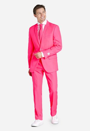Felroze pak met een gestructureerde blazer en rechte broek, gecombineerd met een bijpassende stropdas. Gestyled met witte sneakers en een frisse witte blouse.
