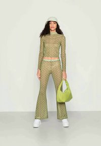 Top de mangas longas em malha com padrão verde e calças flared, combinados com ténis brancos, uma bolsa verde clara e um boné a condizer.