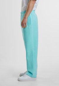 Light blue sweatpants with a relaxed fit, elastic waistband, side pockets, and soft fleece texture, paired with white sneakers.