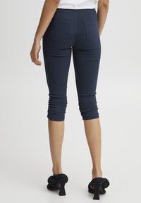 Tamsiai mėlynos, trumpintos leggingos su raukinių detalėmis apatinėje dalyje ir dviem galinėmis kišenėmis, derinamos su juodais aukštakulniais sandalais.