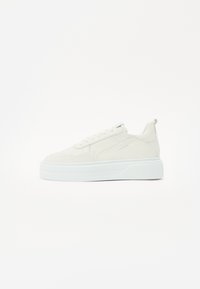 Baskets blanches avec une tige en daim texturé, des accents lisses, un design à lacets et une épaisse semelle en caoutchouc blanche. Comprend une languette à l'arrière.