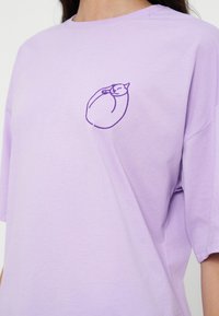 T-shirt oversize lilas avec un petit contour brodé violet d'un chat endormi recroquevillé sur la poitrine gauche.