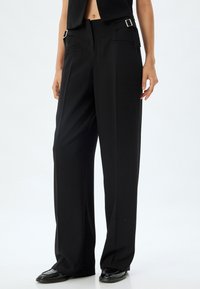Zwarte wijde broek met een maatwerk pasvorm, voorzien van elegante zijzakken en zilveren hardwareaccenten op de tailleband. Glad tekstuur van de stof.