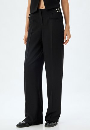 Pantalons larges noirs avec une coupe ajustée, dotés de poches latérales élégantes et d'accents en métal argenté au niveau de la taille. Texture du tissu lisse.