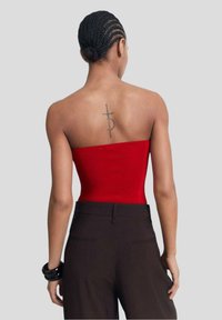 Röd strapless topp i ribbat tyg med en figurnära design. Bärs med mörka byxor och visar en tatuering på ryggen.