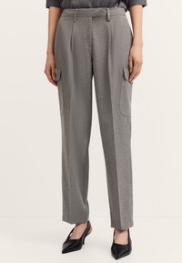 Graue, maßgeschneiderte Hosen aus strukturiertem Stoff, mit seitlichen Cargo-Taschen, geradem Bein und einer taillierten Taille. Kombiniert mit schwarzen, spitzen Schuhen.