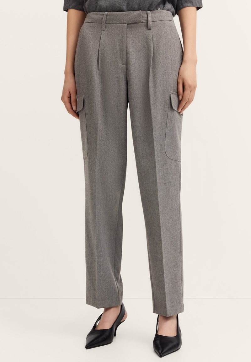 Graue, maßgeschneiderte Hosen aus strukturiertem Stoff, mit seitlichen Cargo-Taschen, geradem Bein und einer taillierten Taille. Kombiniert mit schwarzen, spitzen Schuhen.