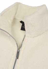 Lichtbeige fleecejack met hoge kraag en metalen rits. De binnenstof is glad. Heeft een label met de merknaam.