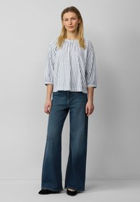 Blusa a righe, blu chiaro e bianco, con pieghe e maniche 3/4; abbinata a jeans svasati blu scuro e scarpe nere.