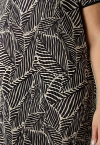 Svart och beige tyg med ett bladmönster som har växlande randiga och släta sektioner, med en textur som har en lätt lyster.