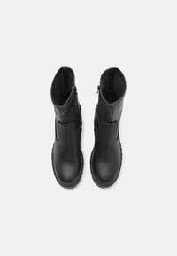 Paire de bottes en cuir noir mi-mollet, bouts ronds, fermetures éclair latérales et semelles épaisses à crampons, vue de dessus.