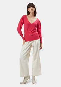 Maglione rosso lavorato a maglia con scollo a V, maniche lunghe e vita aderente. Abbinato a pantaloni a gamba larga beige e stivaletti con tacco lucidi color crema.