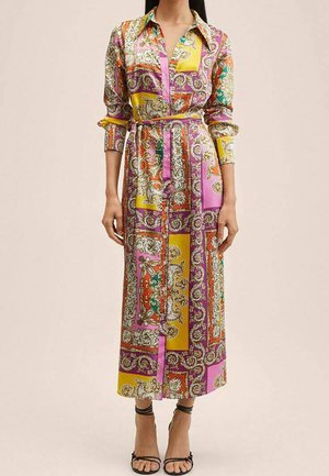 Femme portant une robe à manches longues, ceinturée et boutonnée, avec des motifs patchwork colorés en rose, jaune, orange et violet de type cachemire.