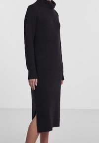 Abito a dolcevita nero realizzato in un morbido materiale a maglia, con maniche lunghe e uno spacco laterale, dal fit rilassato che arriva a metà polpaccio.