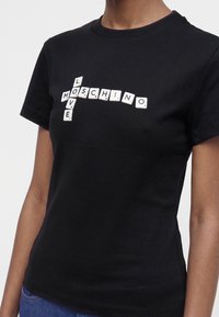 Μαύρο T-shirt με λευκά πλακίδια γραμμάτων σε στυλ Scrabble που σχηματίζουν τις λέξεις "MOSCHINO" και "LOVE" σε διάταξη σταυρολέξου στο στήθος.