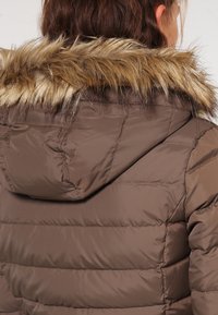 Brązowa kurtka puchowa z kapturem z sztucznego futra, z poziomym pikowaniem i gładką, błyszczącą teksturą. Widok z tyłu pokazuje detale kaptura.