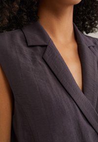 Mörklila ärmlös kavaj med djup V-ringning, texturerad tyg och skarpa slag. Fokusera på minimalistisk design och rena linjer.