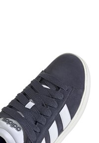 Mörkgrå mockaskor med vita ränder, texturerade skosnören, rund tå och gummisula med en logotyp på utsidan.