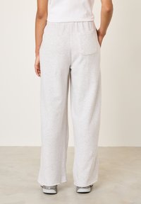 Gaiši pelēkas, plaša piegriezuma sporta bikses ar elastīgu jostu un aizmugurējo kabatu, izgatavotas no mīksta materiāla. Kombinētas ar pelēkām sporta kurpēm.